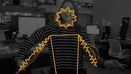 A person in a striped sweater stands in an office while yellow zigzag lines from body tracking trace their head, shoulders and arms.